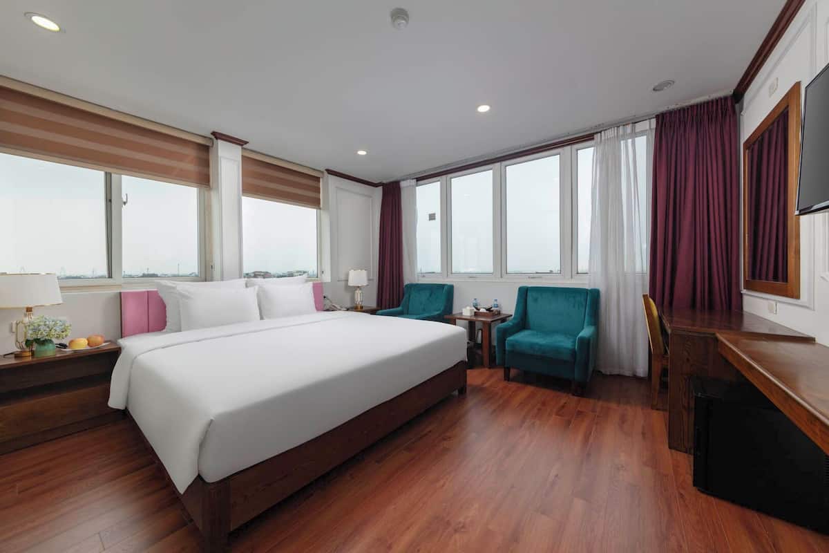 A hotel room with a large bed, two armchairs, a desk, and a TV.