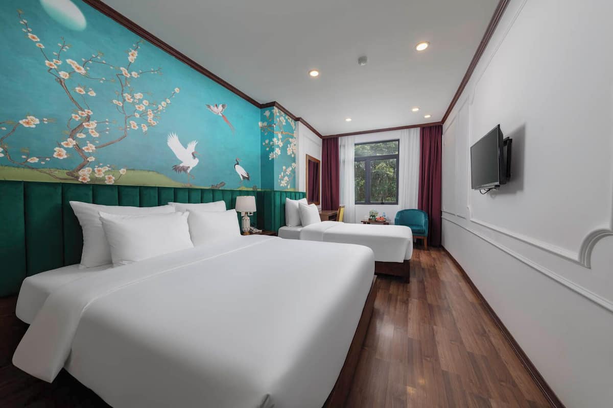 A hotel room with two beds, a mural with birds and flowers, a TV, and a window with a view of greenery.
