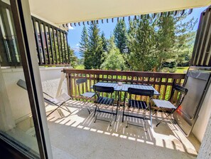 Een balkon met een tafel, stoelen, een barbecue en uitzicht op bomen en een berg.
