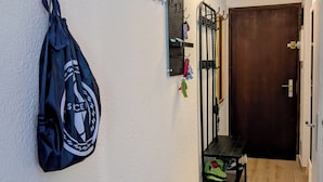 Un couloir avec un porte-manteau, un panneau mural perforé avec des crochets, un banc et une porte.