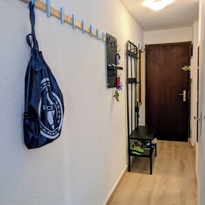 Ein Flur mit Kleiderhaken, einem an der Wand befestigten Wäscheständer mit Haken, einer Bank und einer Tür.