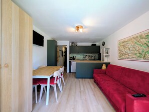 Un espacio habitable compacto con comedor, kitchenette y un sofá rojo.