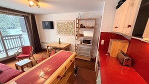 Une pièce compacte comprenant une table à manger, des chaises, un petit coin cuisine avec un four à micro-ondes et un téléviseur fixé au mur.
