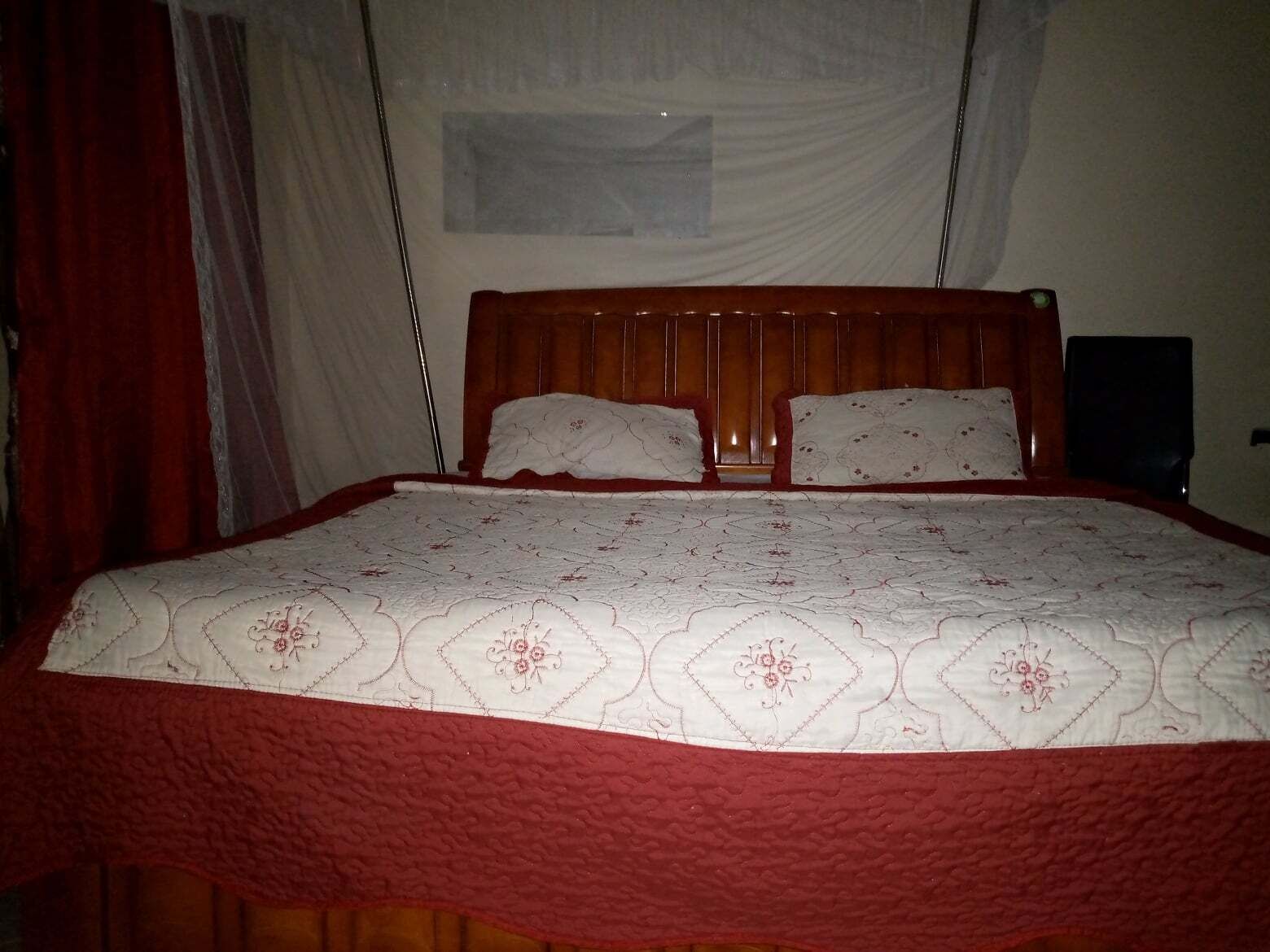 A bed with a wooden headboard, two pillows, and a red quilt.