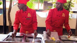 Zwei Köche in roten Uniformen bereiten Speisen an einem Buffet zu.