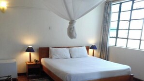 Ein Schlafzimmer mit einem hölzernen Bett, zwei Nachttischlampen, einem Nachttisch, einem Fenster mit Vorhängen und einem Teppich mit Sonnendruck.