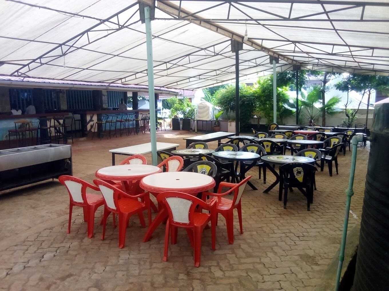 Un espace extérieur aménagé en terrasse, avec des tables et des chaises rondes, un barbecue et un coin salon abrité.