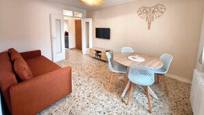 Ein Wohnzimmer mit Sofa, einem Esstisch mit Stühlen, einem an der Wand montierten Fernseher und einem Wandbild.