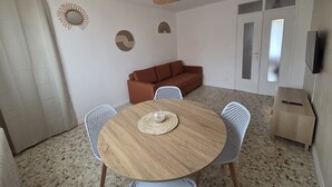 Ein Essbereich mit einem runden Holztisch, weißen Stühlen, einem braunen Sofa und einem Deckenventilator.