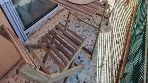 Ein Balkon mit Glastür, einem Holztisch mit gewebter Matte und einem Stuhl.
