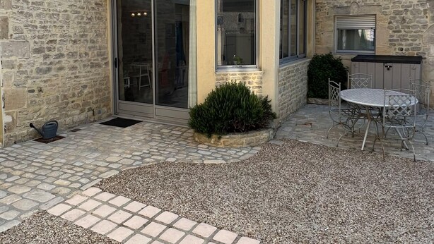 Un edificio de piedra con puerta de vidrio, un pequeño balcón y un patio con mesa y sillas.