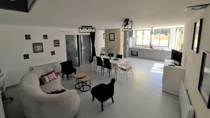 Una sala moderna con un sofá curvo, un comedor con mesa y sillas, una cocina con ventana y una escalera que sube a un nivel superior.