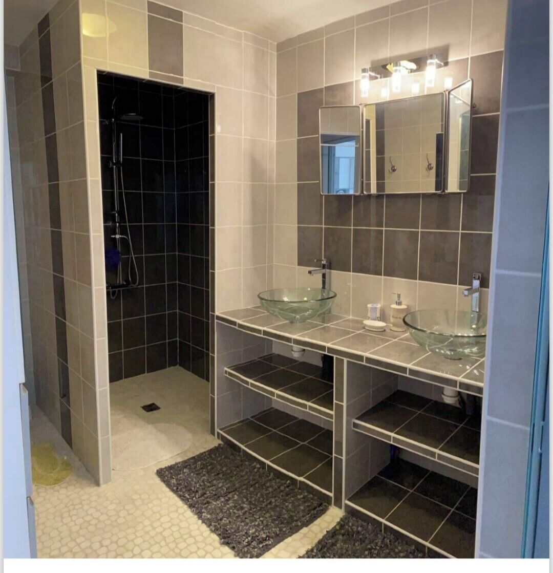 A modern bathroom with two glass sinks, a walk-in shower, and a mirror above the sink.