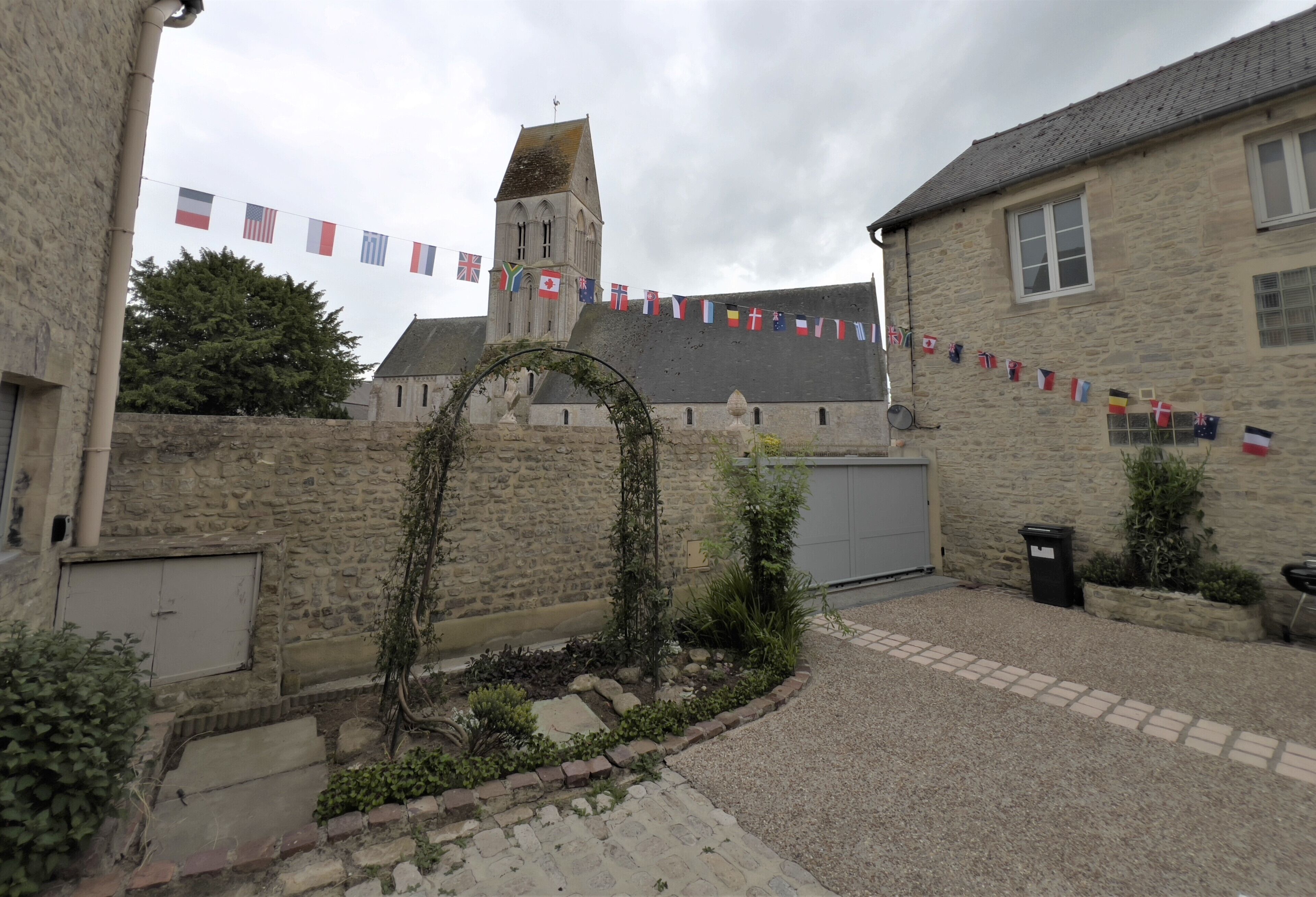 A stone building with a tower, surrounded by cobblestone paths and a garden with ivy. Flags are strung across the top of the tower.