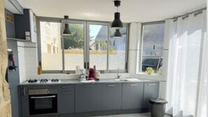 Una cocina moderna con armarios grises, horno integrado, un lavamanos y una ventana con vista a una casa y un coche.