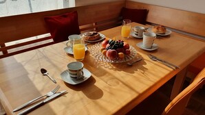 Aamiaispöydällä on hedelmäkulho, lasi appelsiinimehua ja lautanen, jossa on leivonnaisia.