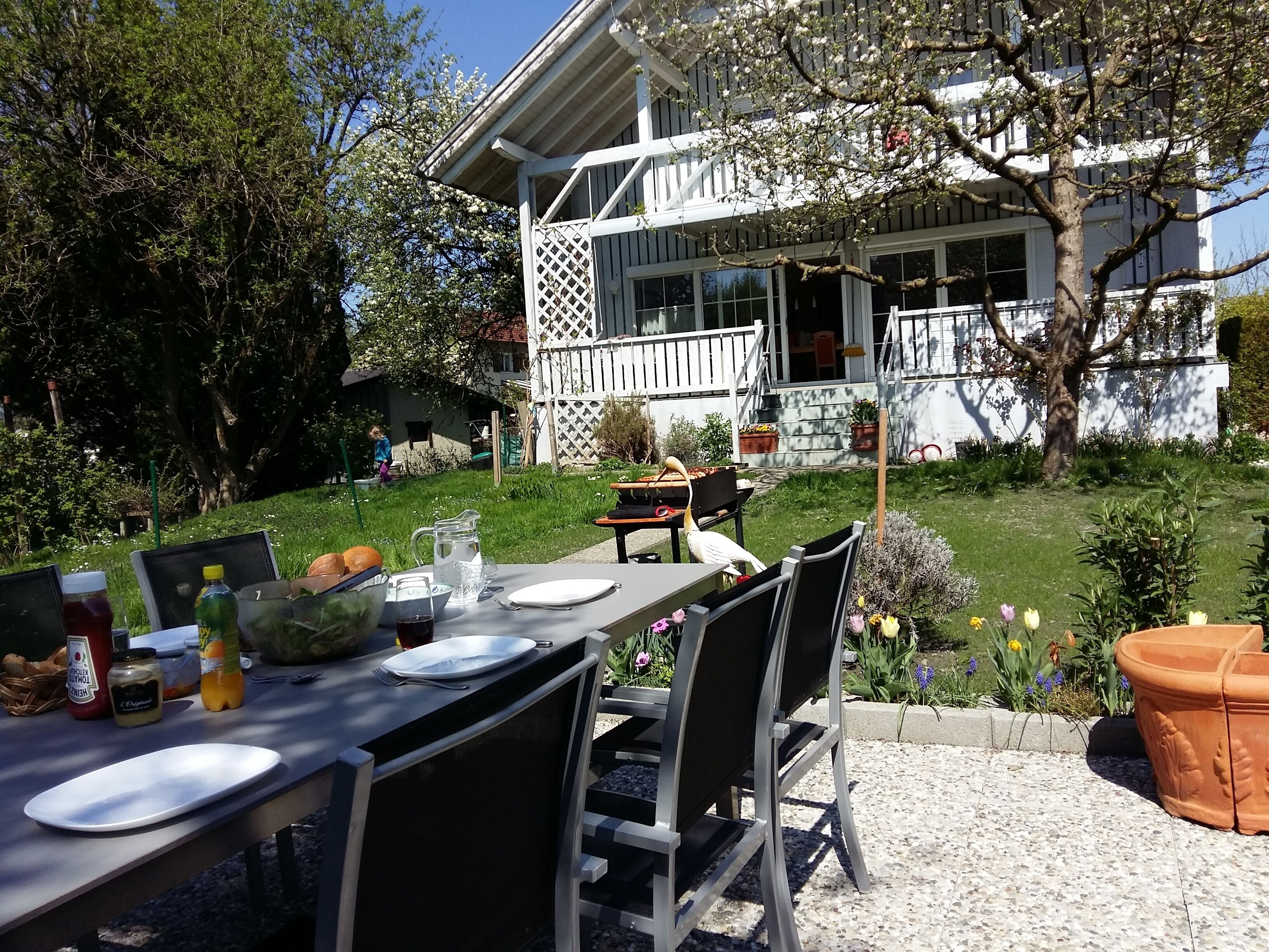 An outdoor dining area with a table set for two, surrounded by chairs, a pitcher, and condiments.