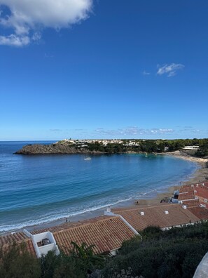A coastal view with a beach, a rocky outcrop, and a small sailboat. - Apartment 'Dreams Of Menorca' with Sea View, Shared Pool, and Wi-Fi (Arenal des Castell)