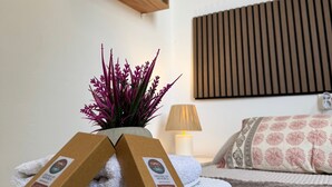 A neatly arranged bedroom with a bed, a bedside lamp, a wall-mounted shelf with decorative items, and a potted plant. - Apartment 'Dreams Of Menorca' with Sea View, Shared Pool, and Wi-Fi (Arenal des Castell)
