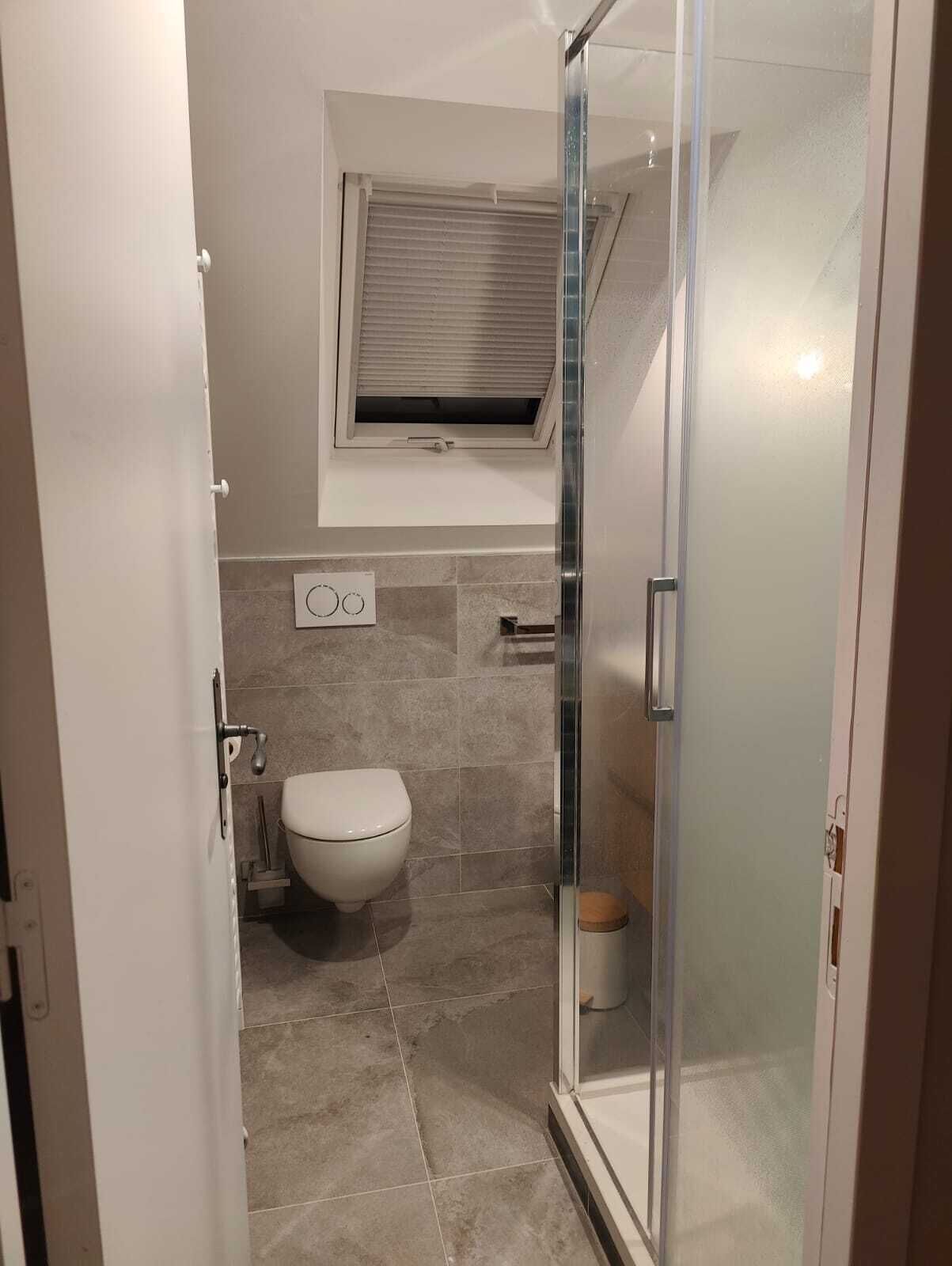 Ein kleines Badezimmer mit Toilette, Dusche und einem Fenster über der Toilette.