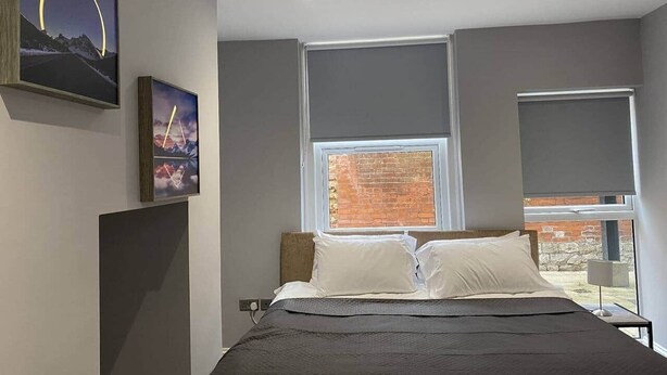 Un dormitorio moderno con una cama grande, dos ventanas y obras de arte en las paredes.