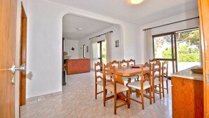 Comedor con mesa y sillas de madera, mostrador de cocina y vista a zonas verdes.