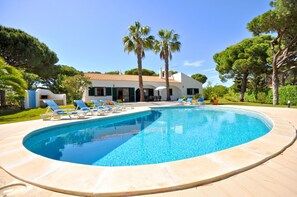 A swimming pool with lounge chairs, a house with a tiled roof, and palm trees. - Casa da Palmeira in Quarteira (Loulé)