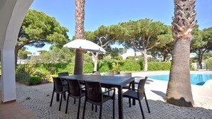 Un patio al aire libre con mesa y sillas, una piscina y palmeras.