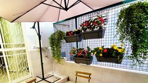 Een terras buiten met een houten tafel en stoelen, een grote parasol en planten in potten op een betegelde muur.