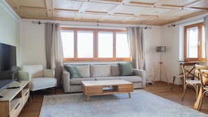 A spacious living room with a wooden ceiling, a sofa set, a coffee table, and a television. - ღLiboria | Aidling Panorama house with mountain view (Riegsee)