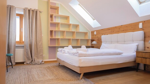 A bedroom with a sloped ceiling, a skylight, a bed with white linens, a wooden headboard, and built-in shelving. - ღLiboria | Aidling Panorama house with mountain view (Riegsee)