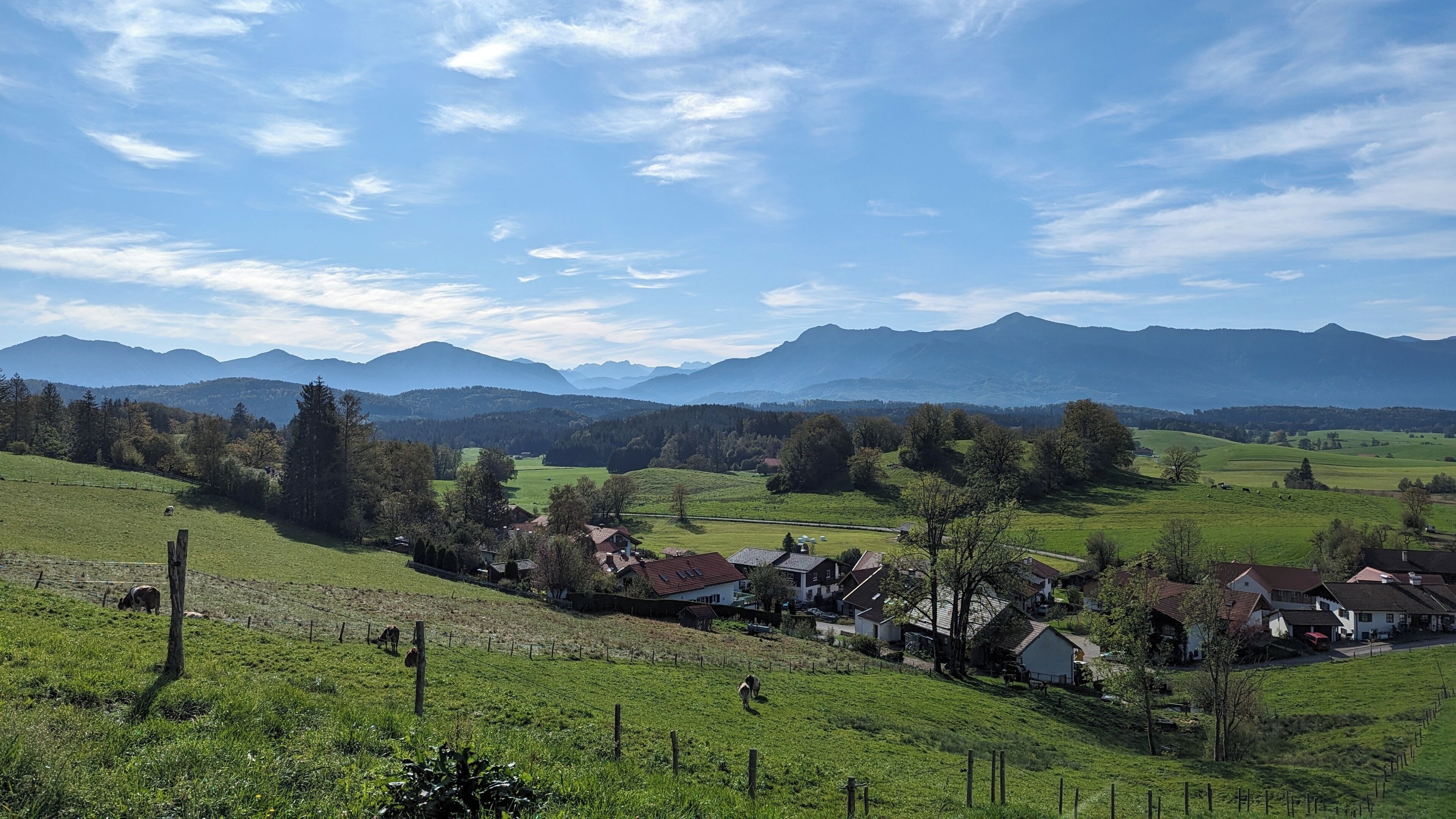 A rural landscape with houses, a fence, and mountains in the background.