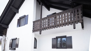 A building with a white exterior, dark wooden balcony railing, and multiple windows with dark shutters. - ღLiboria | Aidling Panorama house with mountain view (Riegsee)