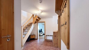 A hallway with a wooden staircase, a wooden cabinet with hooks, and a tiled floor. - ღLiboria | Aidling Panorama house with mountain view (Riegsee)