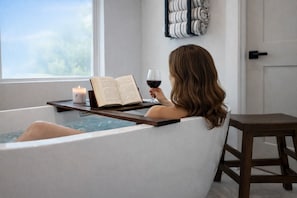 A person relaxing in a bathtub with a book and a glass of wine, a candle, and a view of the outdoors. - Bahia Vista Wellness House w/ heated pool, spa, sauna, garage gym. (Sarasota)