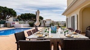 A dining area with a pool, outdoor furniture, and a table set for a meal. - Villa Brady (Olhos de Água)