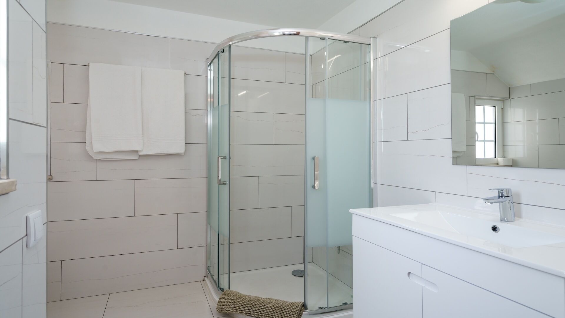 A modern bathroom with a glass shower enclosure, white tiles, and a large mirror.