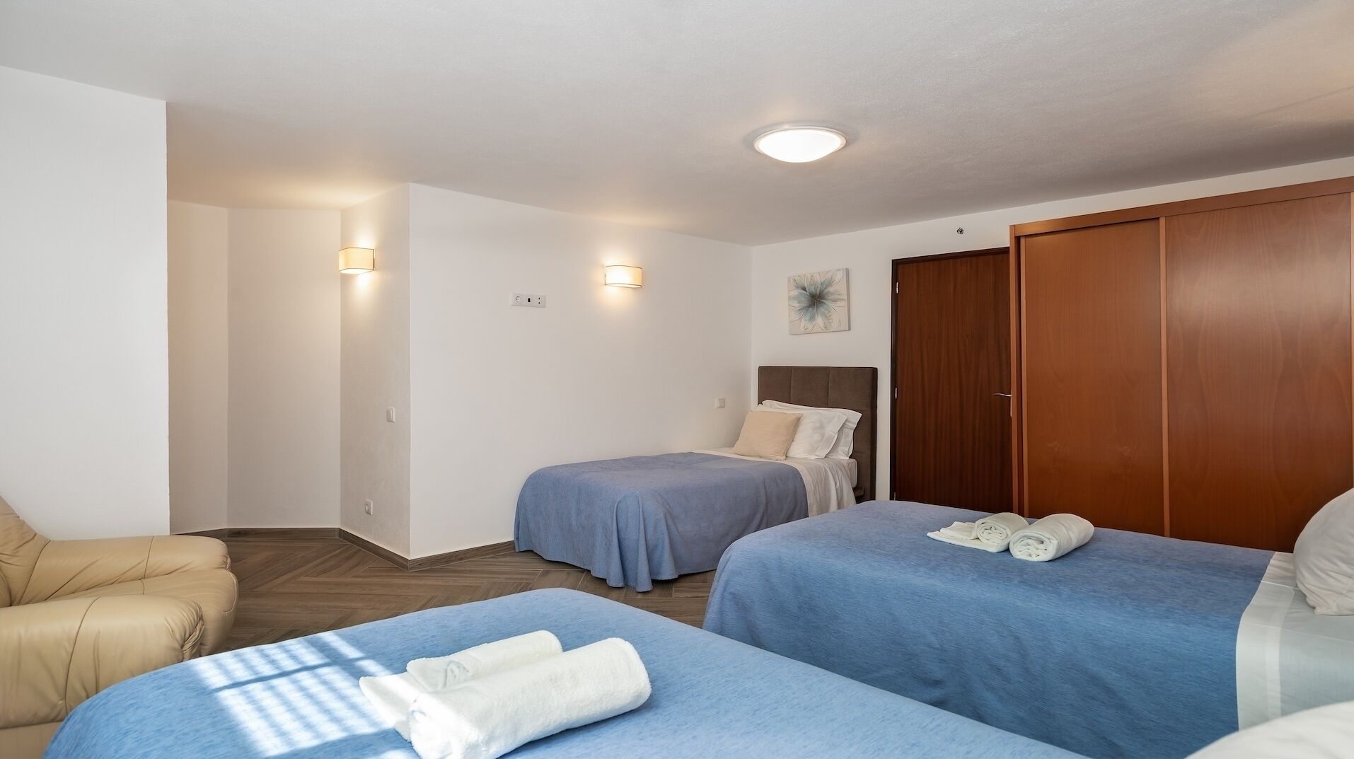 A hotel room with two single beds, a wooden wardrobe, a sofa, and a small table.