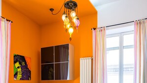 A dining area with a white table and chairs, a colorful chandelier, and a large window with curtains. - Casa al rettifilo con Terrazzo (Naples)