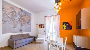 A living room with a large world map, a white sofa, a dining table with chairs, and a colorful painting on the wall. - Casa al rettifilo con Terrazzo (Naples)