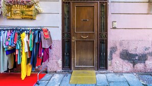 A storefront with a large wooden door, a metal gate, and a variety of colorful clothing items displayed outside. - Casa al rettifilo con Terrazzo (Naples)
