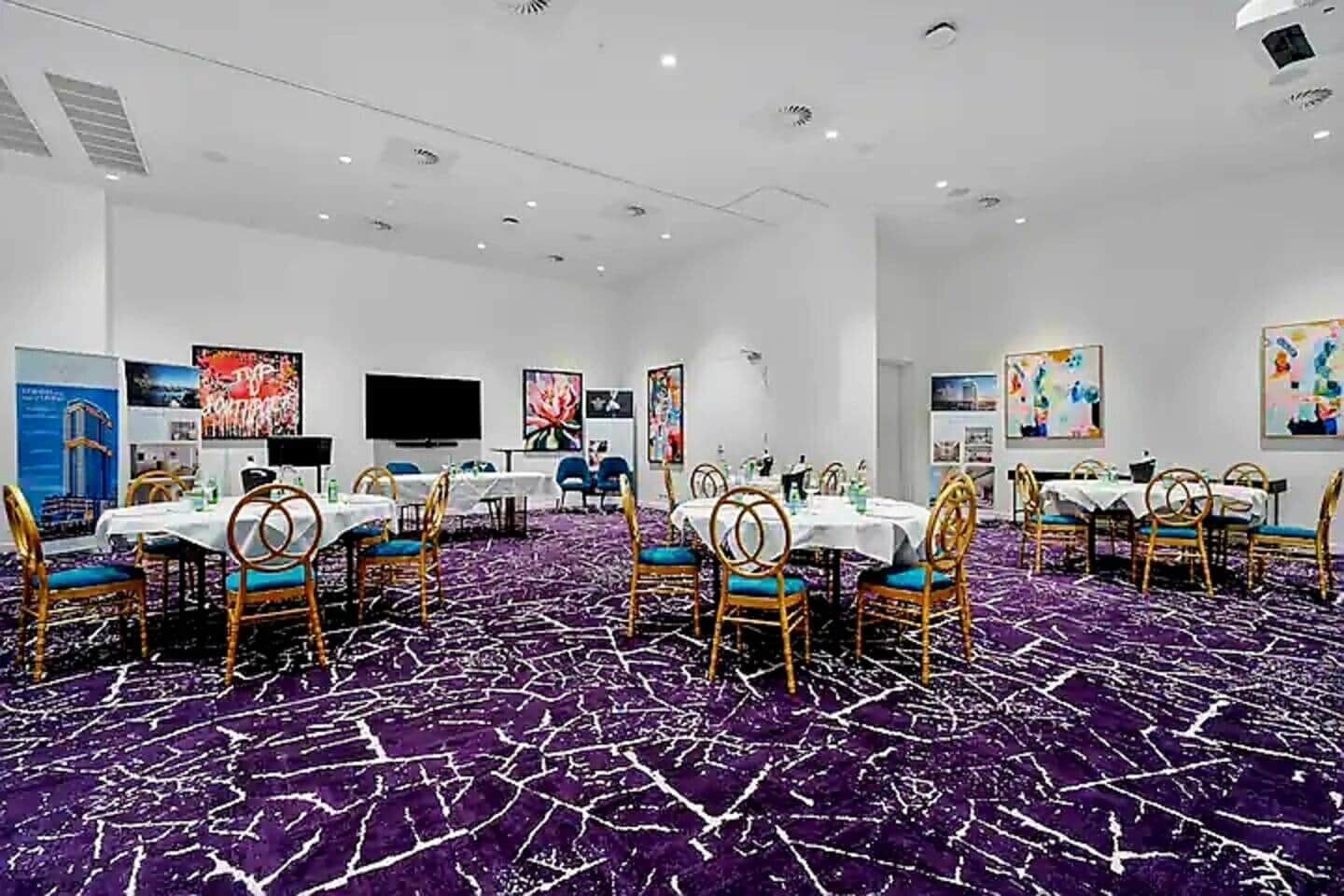 Une salle de conférence équipée de tables rondes, de chaises et d’un grand écran.