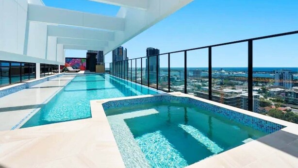 Ein Infinity-Pool auf dem Dach mit Blick auf die Stadt, umgeben von Glasgeländern und moderner Architektur.