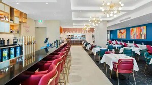 Ein modernes Restaurant mit einer langen Bar, roten Barhocker und verschiedenen Sitzmöglichkeiten, darunter Tische und Stühle.