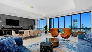 Ein geräumiger Wohnbereich mit modernem Design, ausgestattet mit einem großen Fenster mit Blick auf die Stadt, bequemen Sitzgelegenheiten und einem an der Wand montierten Flachbildfernseher.