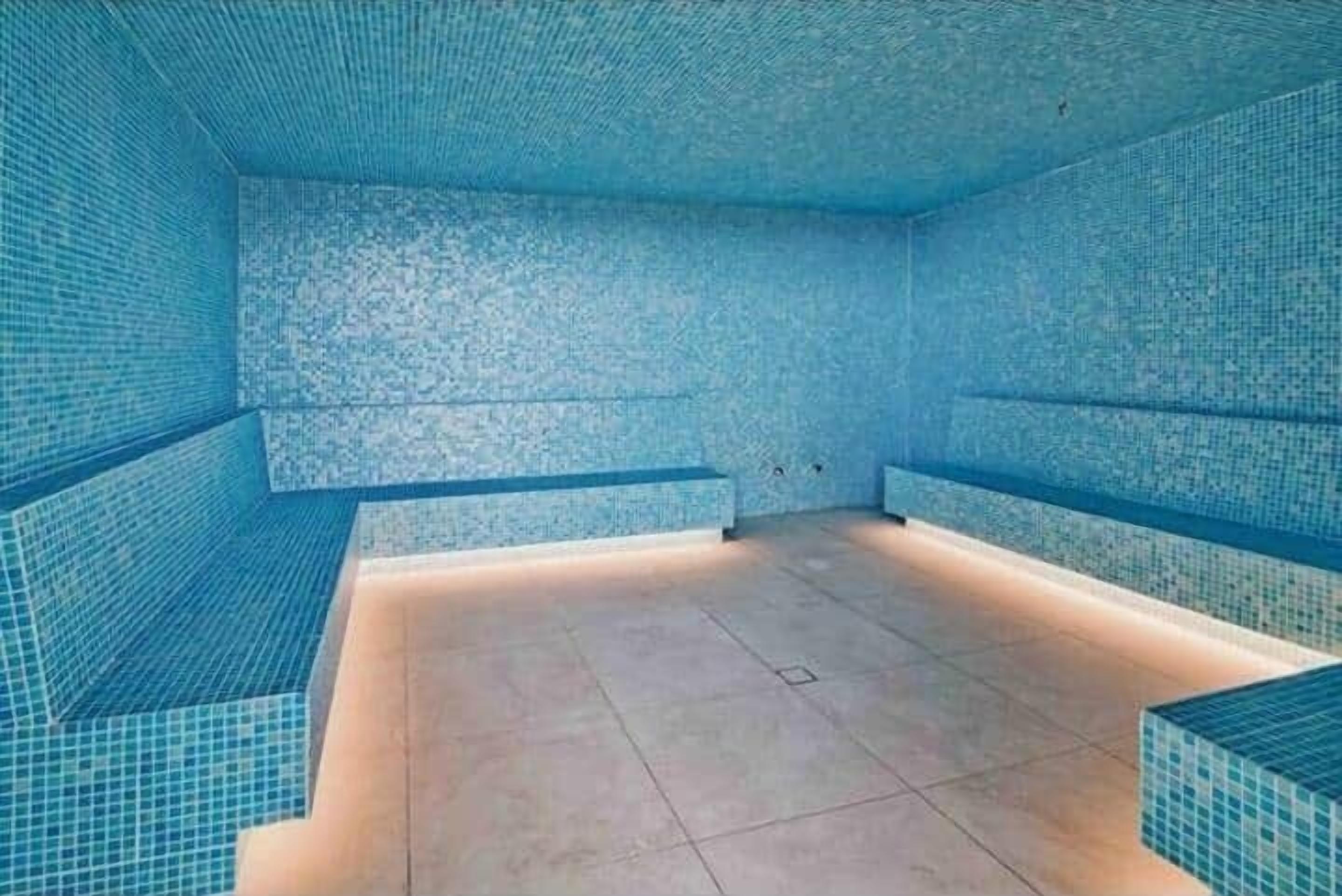 Ein Schwimmbecken mit gefliesten Wänden und einem gefliesten Boden, mit einer Sitzbank entlang einer Seite.