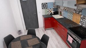 Een compacte keuken met een eethoek, met een ronde tafel met stoelen, een rode kast en een zwart aanrecht.