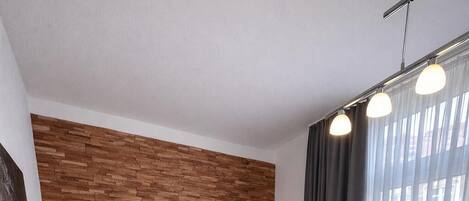 A modern bedroom with a wooden headboard, a large bed with two pillows, a bedside table, and a window with curtains.