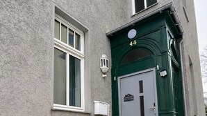 Een gebouw met een grijze, structuurrijke gevel, een groene deur met het nummer 44, en een klein raam aan de linkerkant.