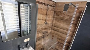 Een moderne badkamer met een glazen douchecabine, een wastafel met spiegel en houten vloer.